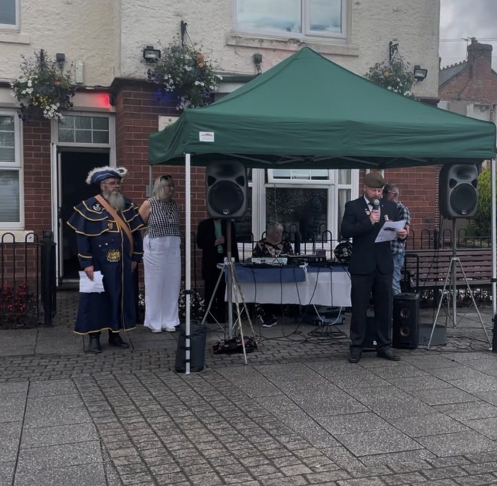 A photograph of the Veteran reading a poem, with the Mayor and the Town Crier in the background