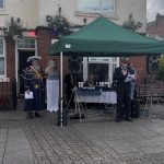 A photograph of the Veteran reading a poem, with the Mayor and the Town Crier in the background